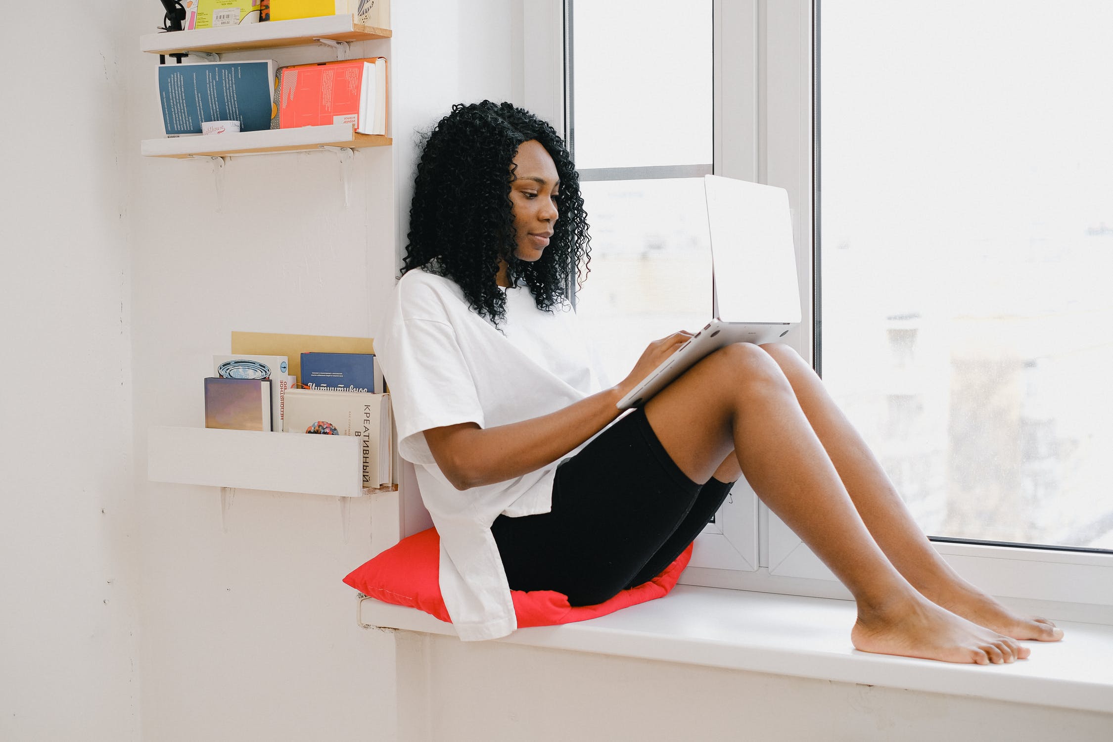 Black woman resting on window sill while using laptop